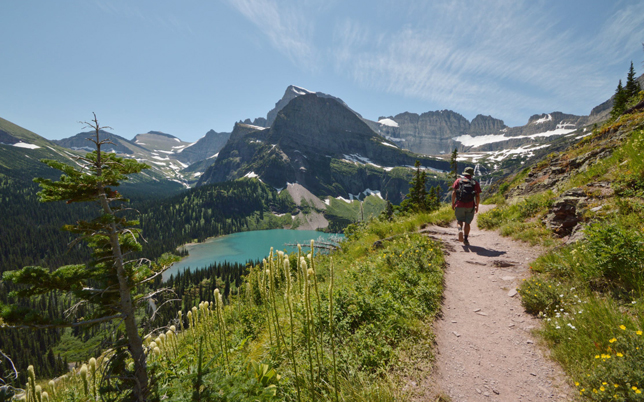 Hiker walking on a trail with mountains and a lake in the background.
